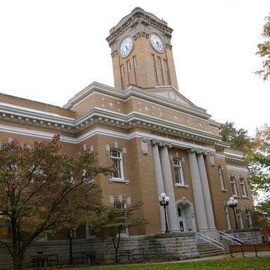 The courthouse in Jackson County Indiana. It is a tan brick building with four off white columns at the front and a tall clock tower.